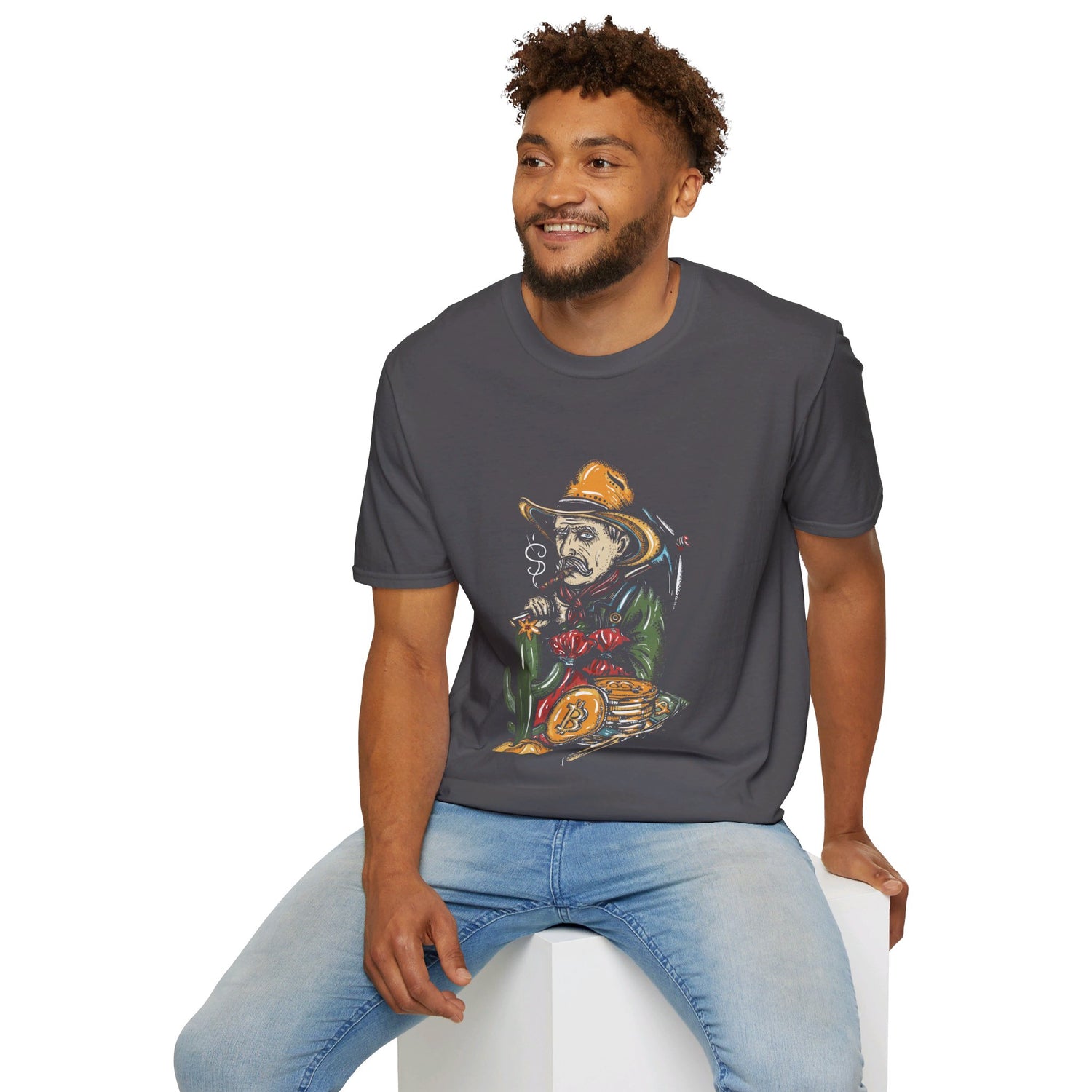 A man sits on a white block, smiling, wearing a dark grey T-shirt with a graphic of a skeleton in a cowboy outfit smoking a cigar and holding a bag of money, with a stack of bitcoin coins