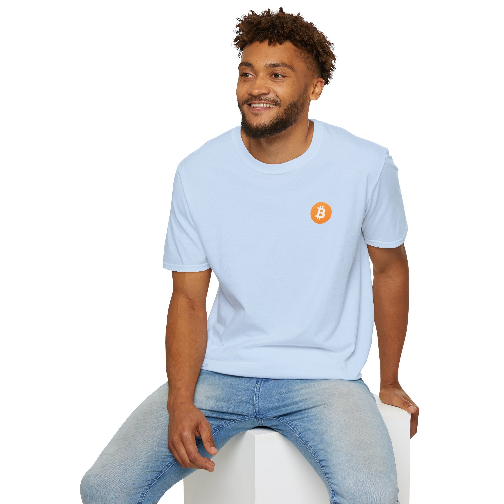 A guy sitting on a white cube smiling wearing a light blue round neck t-shirt with a small orange bitcoin logo on the left chest