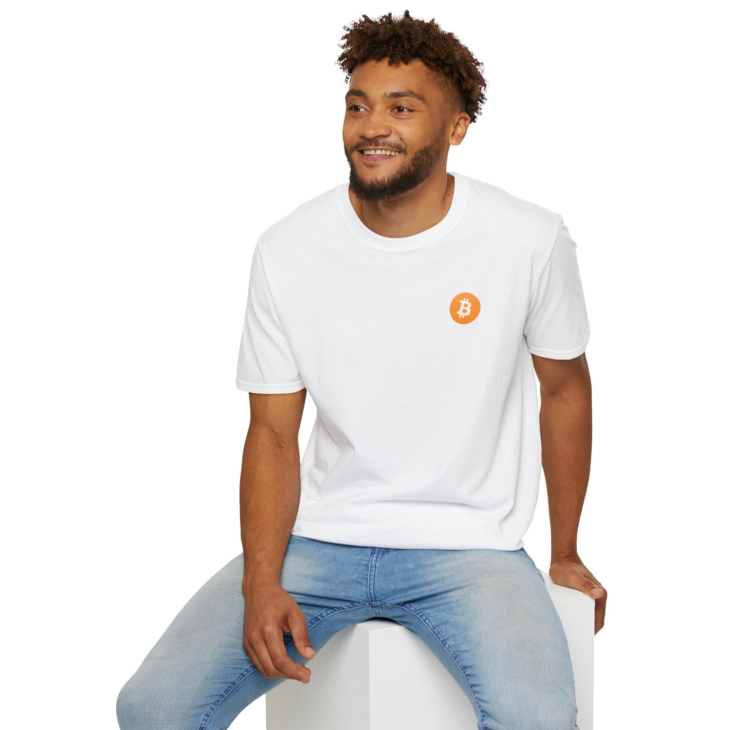 A guy sitting on a white cube smiling wearing a white round neck t-shirt with a small orange bitcoin logo on the left chest