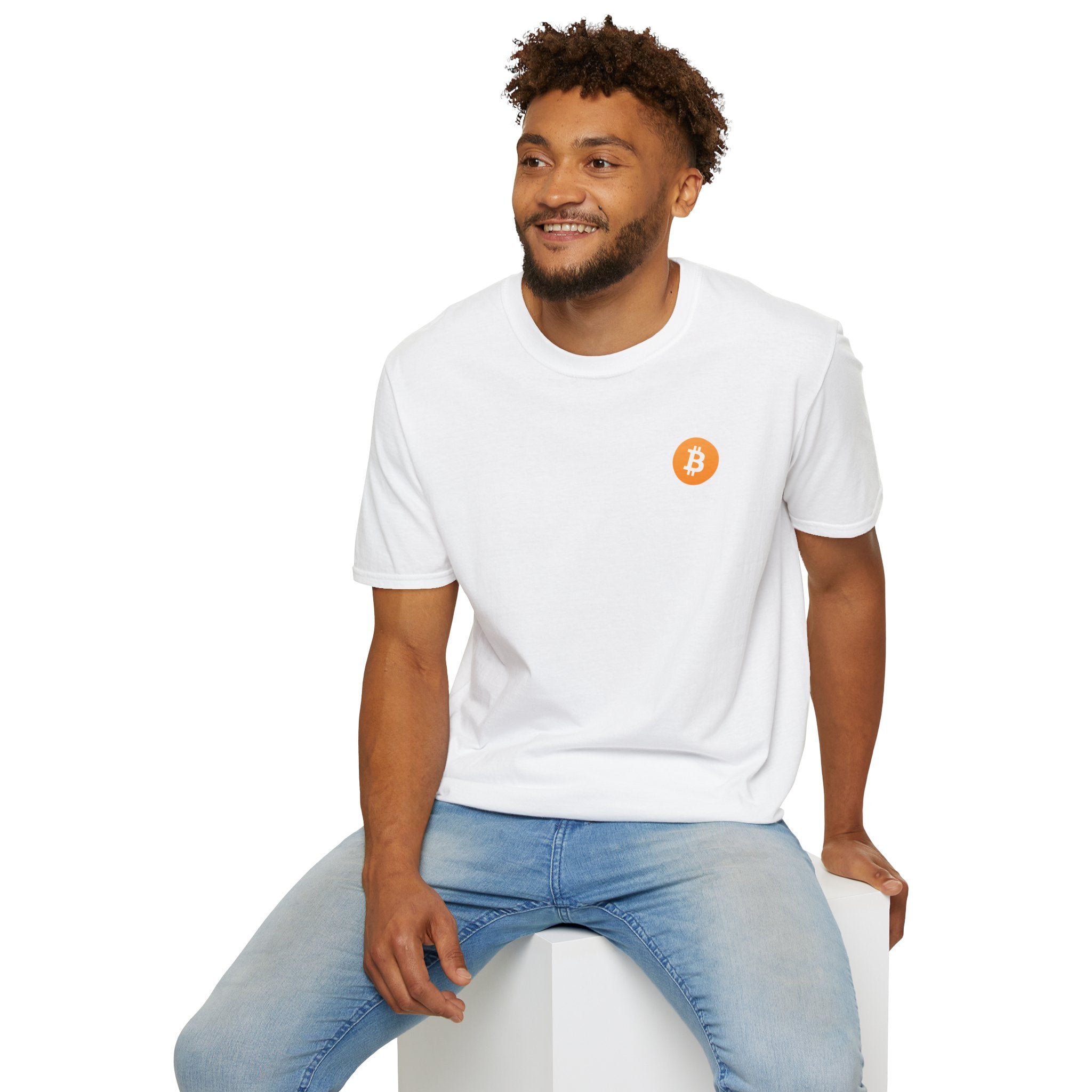 A guy sitting on a white cube smiling wearing a white round neck t-shirt with a small orange bitcoin logo on the left chest