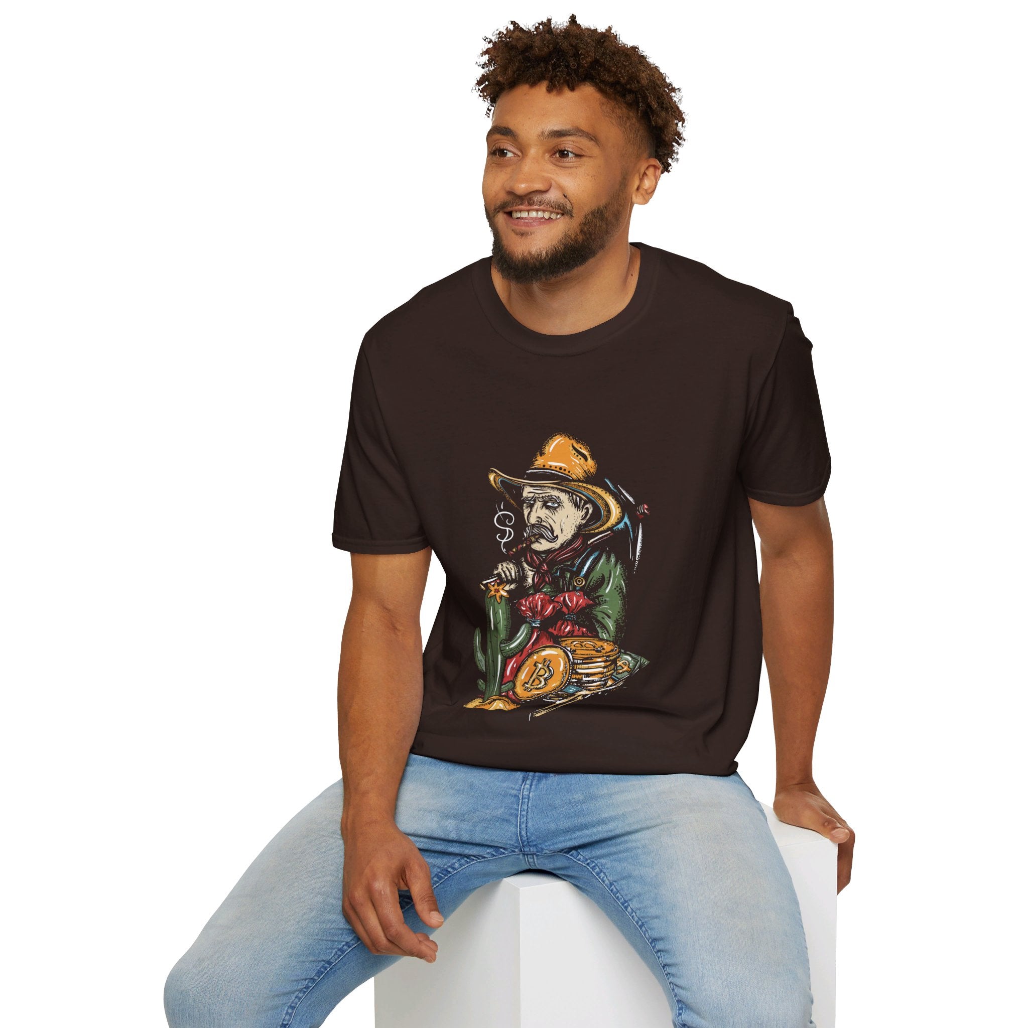 A man sits on a white block, smiling, wearing a brown T-shirt with a graphic of a cowboy smoking a cigar and holding a bag of money,with a stack of bitcoin coins