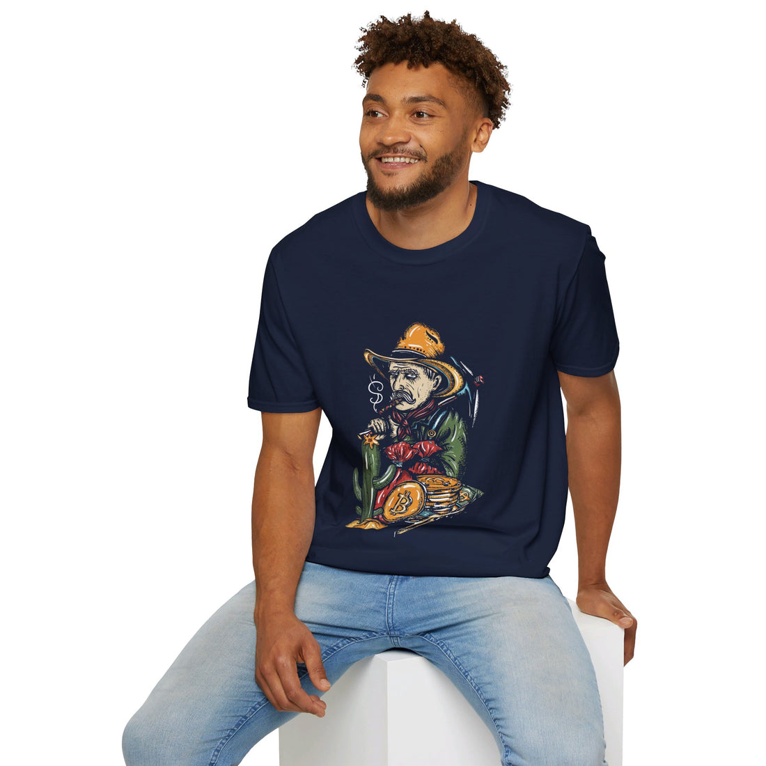 A man sits on a white block, smiling, wearing a navy blue T-shirt with a graphic of a skeleton in a cowboy outfit smoking a cigar and holding a bag of money., with a stack of bitcoin coins